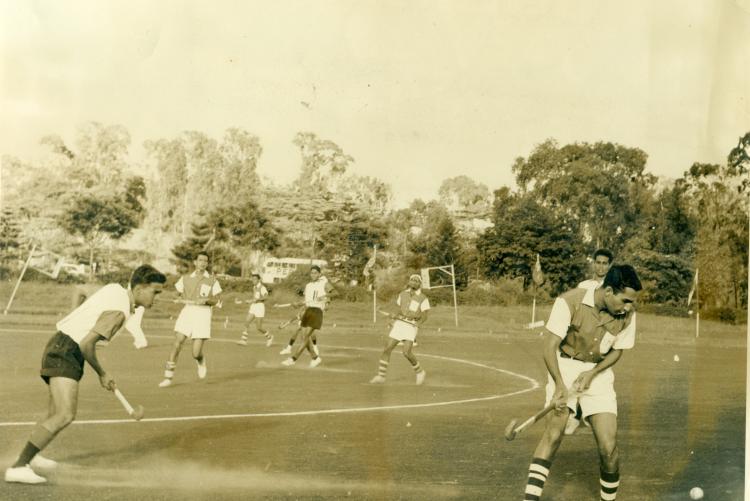 Male students playing hockey in the field 1978.